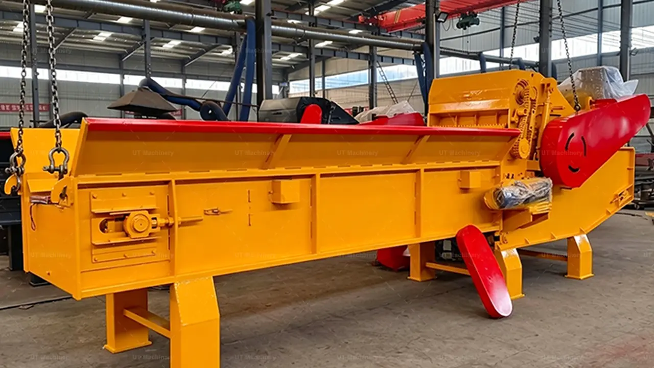 A powerful industrial wood chipper, with a vibrant yellow main structure and striking red accents, stands ready in a large factory bay. Its substantial processing unit, large motor, and rugged chain-plate feeding conveyor define its heavy-duty capacity for high-volume chipping.
