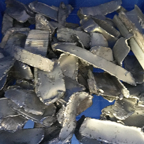 Crushed steel machining shavings in a blue container, reduced to uniform granules by a metal crusher.